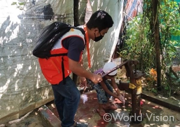担当事業において整備した井戸で、ワールド・ビジョンのボランティアから新型コロナウイルス感染予防のための手洗いについて教わるロヒンギャ難民の男の子