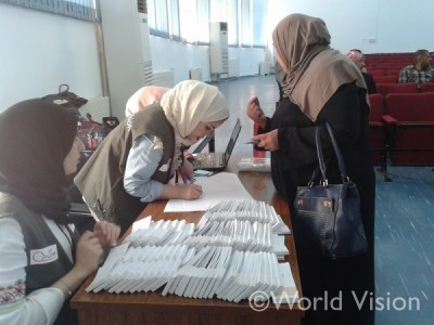 越冬のためのアイテム引換券を渡される難民の女性（右）