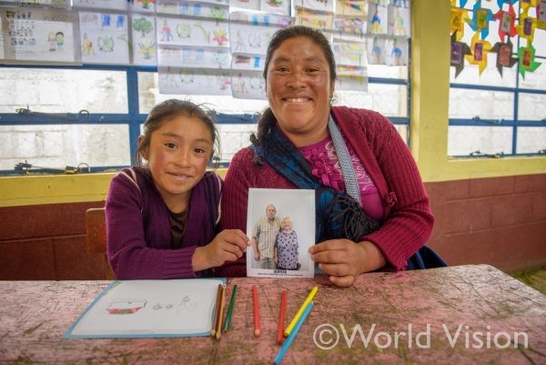 自分で選んだスポンサーの写真を持つグアテマラの女の子とお母さん 