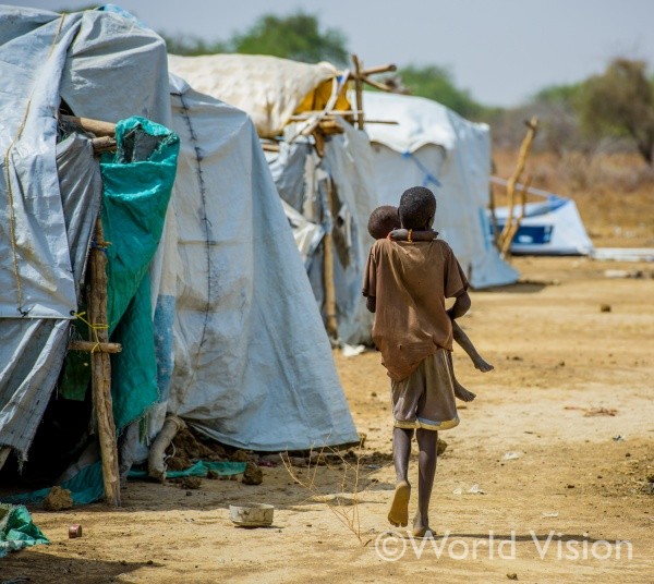 難民キャンプで、弟を抱いて歩く男の子