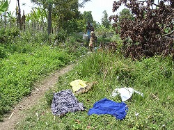 3件目付近の小川で村の女性が洗濯中 -洋服は草の上で乾燥